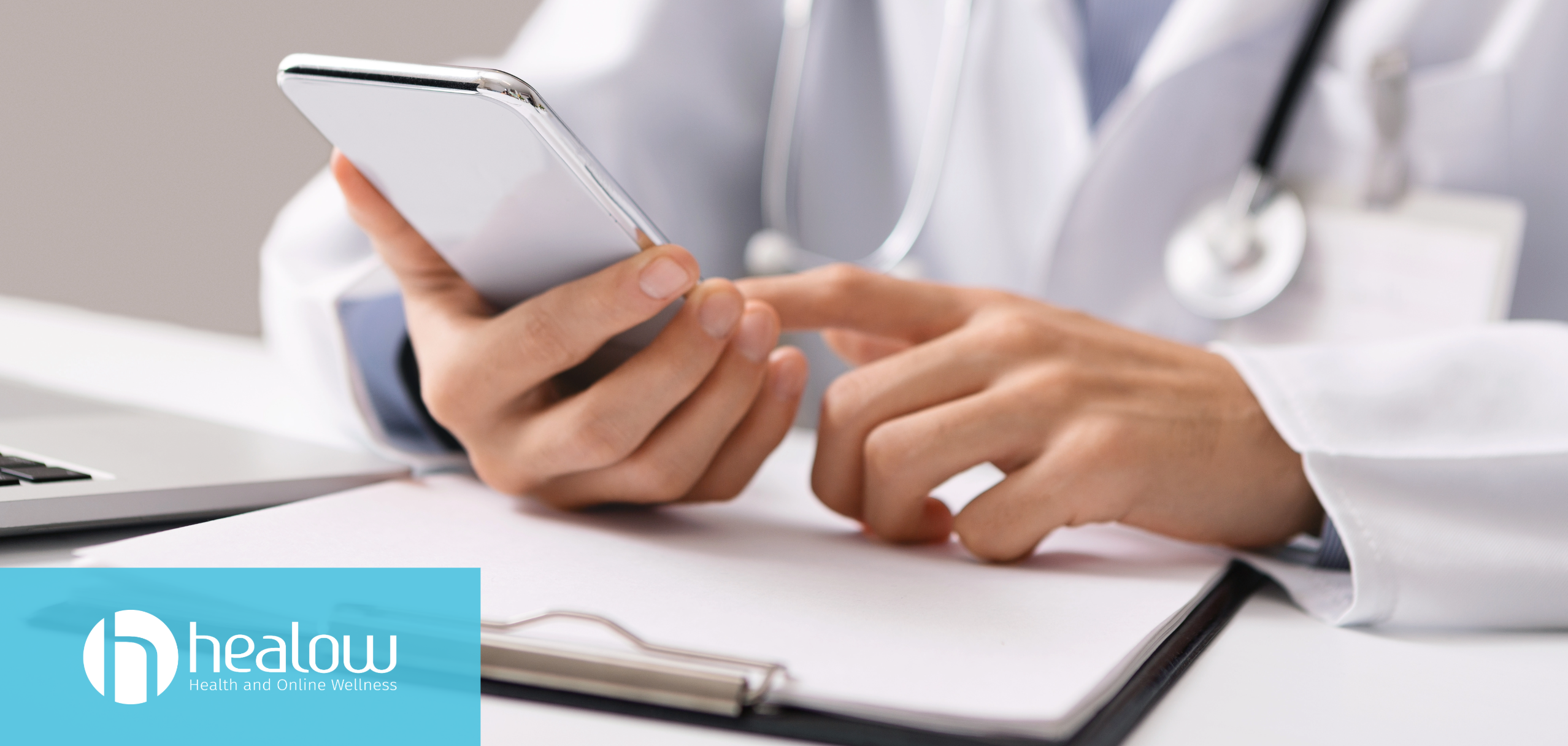 physician holding smartphone engaging with patients. A laptop keyword is seen in the corner and the physician is leaning on a clipboard
